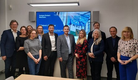 Gruppenbild mit einer Präsentation mit Sachsen- und EU-Flagge im Hintergrund