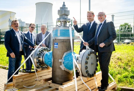 Personen stehen um ein Bauteil einer Wasserstoffleitung, im Hintergrund Kraftwerksgelände mit einem Kühlturm