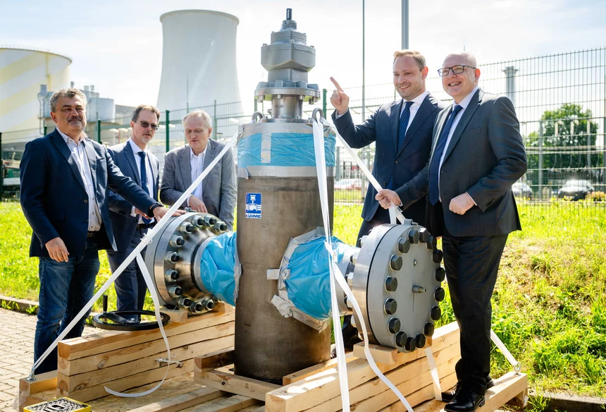 Personen stehen um ein Bauteil einer Wasserstoffleitung, im Hintergrund Kraftwerksgelände mit einem Kühlturm