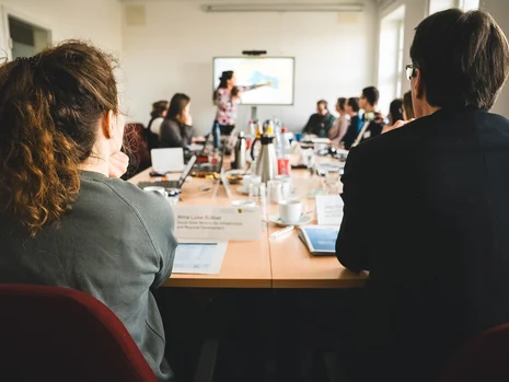 SMIL Personen an einem Konferenztisch, eine Frau hält eine Präsentation