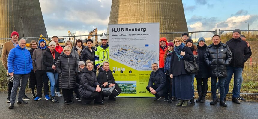 Personen gruppieren sich um ein Plakat zu einem Projekt für erneuerbare Energie, im Hintergrund Kühltürme, welche zur Sprengung vorbereitet sind