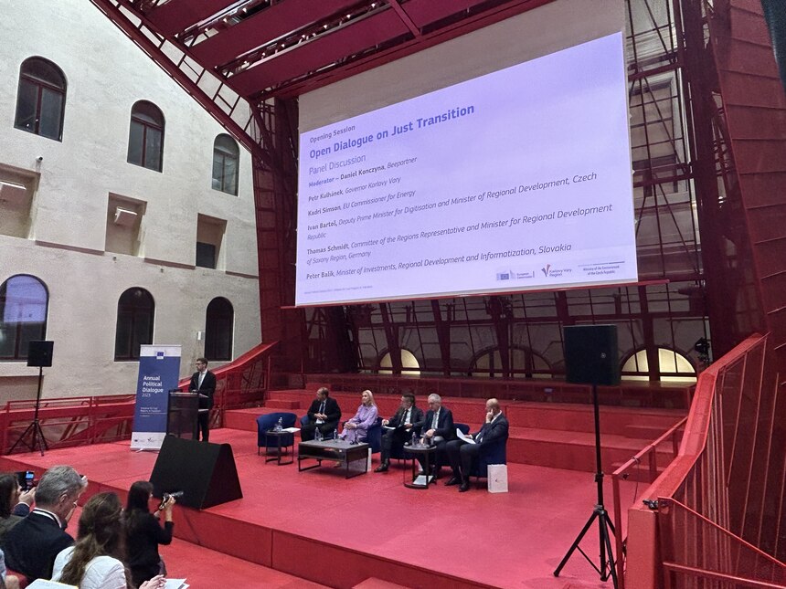 Teilnehmer einer Podiumsdiskussion auf einer Bühne, dahinter eine Präsentation auf einer Leinwand