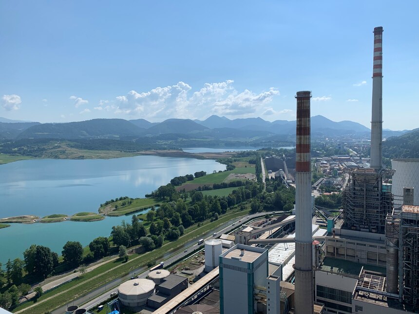 Kraftwerksgelände von oben, im Hintergrund Seen, dahinter Berge und blauer Himmel