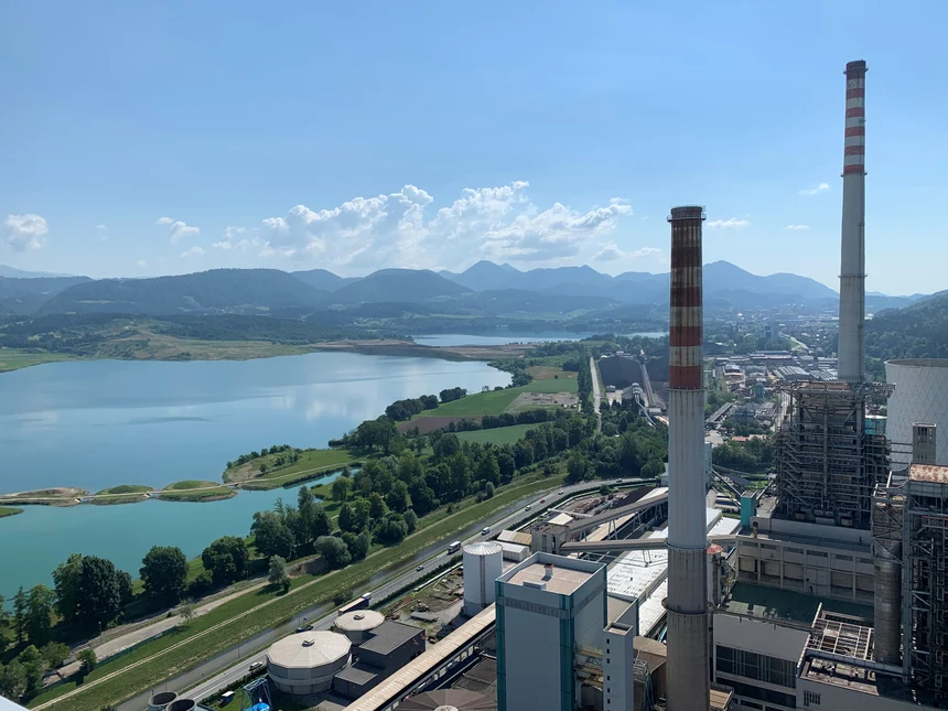Kraftwerksgelände von oben, im Hintergrund Seen, dahinter Berge und blauer Himmel